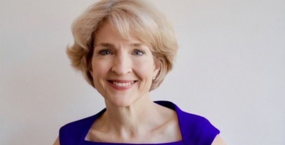An older woman with short blonde hair wears a royal blue dress
