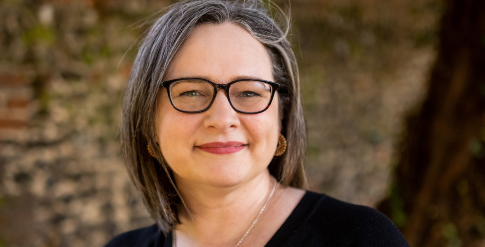 A woman with a dark bob and glasses in a black top smiles at the camera