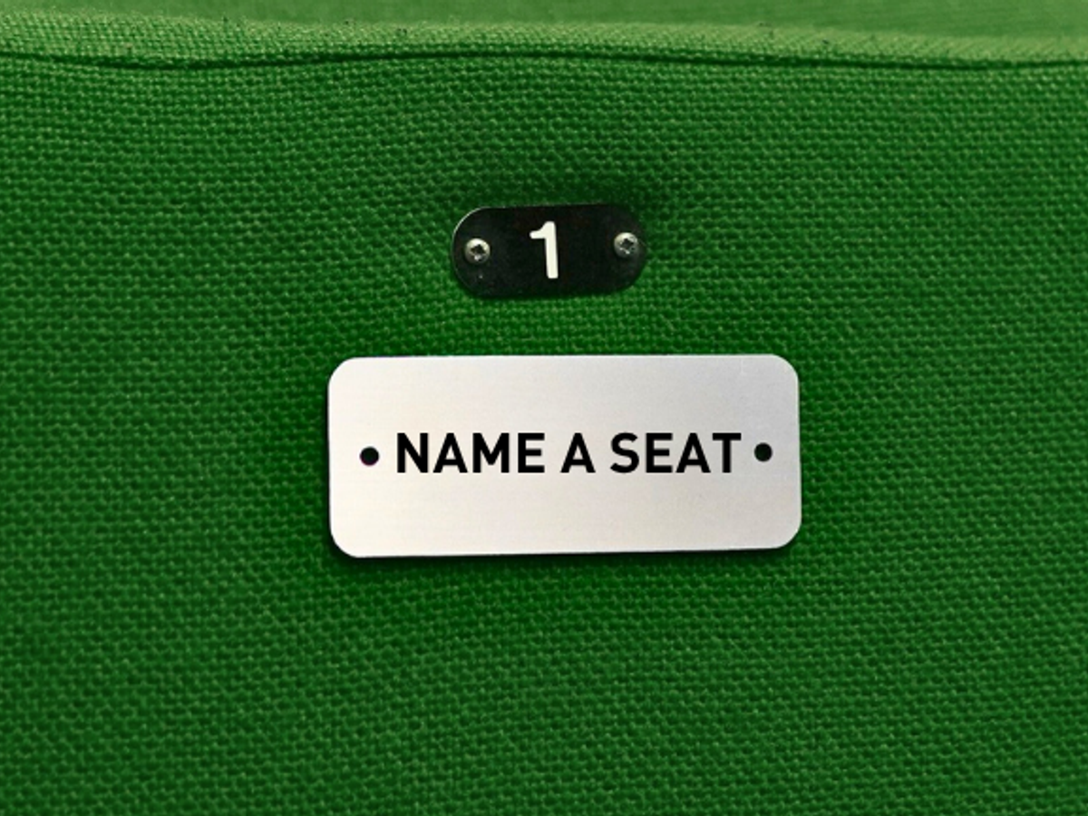 A seat with green fabric and a silver plaque that reads '1' and 'Name a Seat'