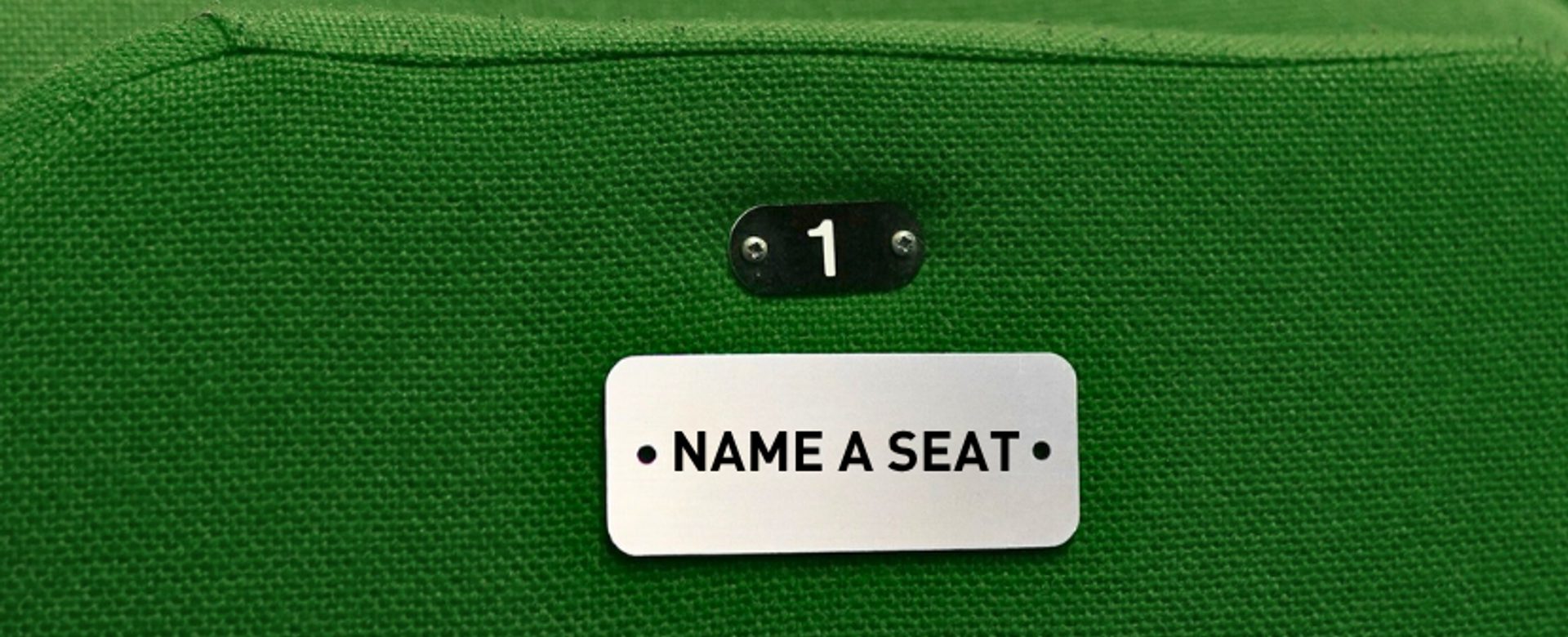 A seat with green fabric and a silver plaque that reads '1' and 'Name a Seat'