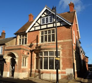 The Old Library, a two story brick building with a bay window and black and white paneling near the roof