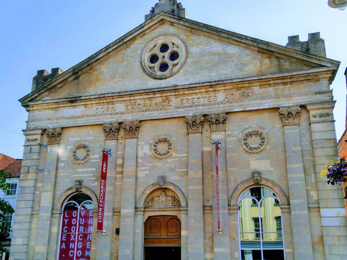 A stone building with a round window at the top and four pillars in the sunshine with blue sky.
