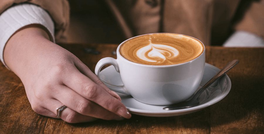 A latte art coffee with a manicured hand holding the cup on a wooden table