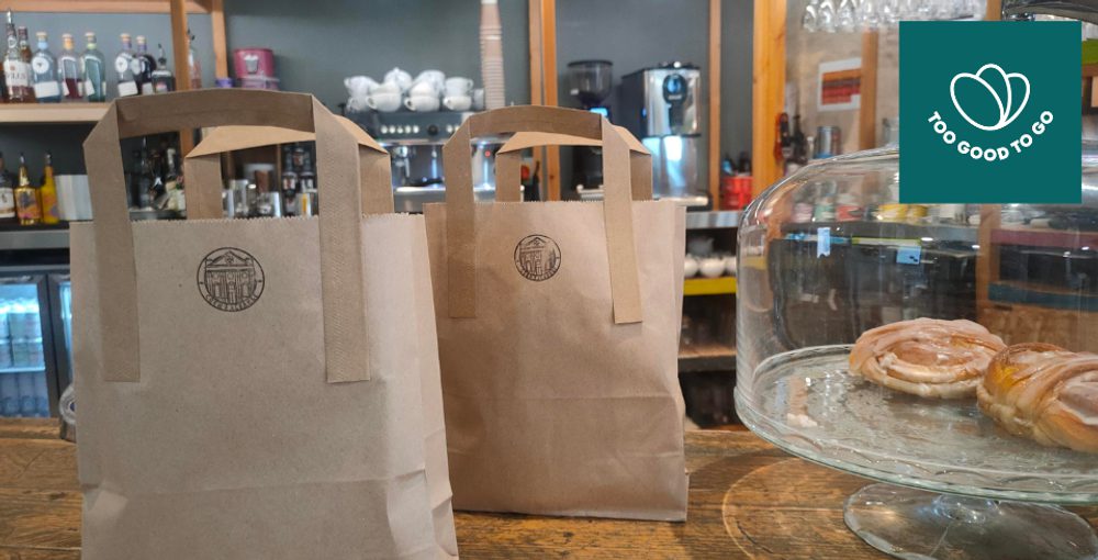 Two brown bags with a stamp of the Corn Exchange on them sit on a counter next to some baked goods