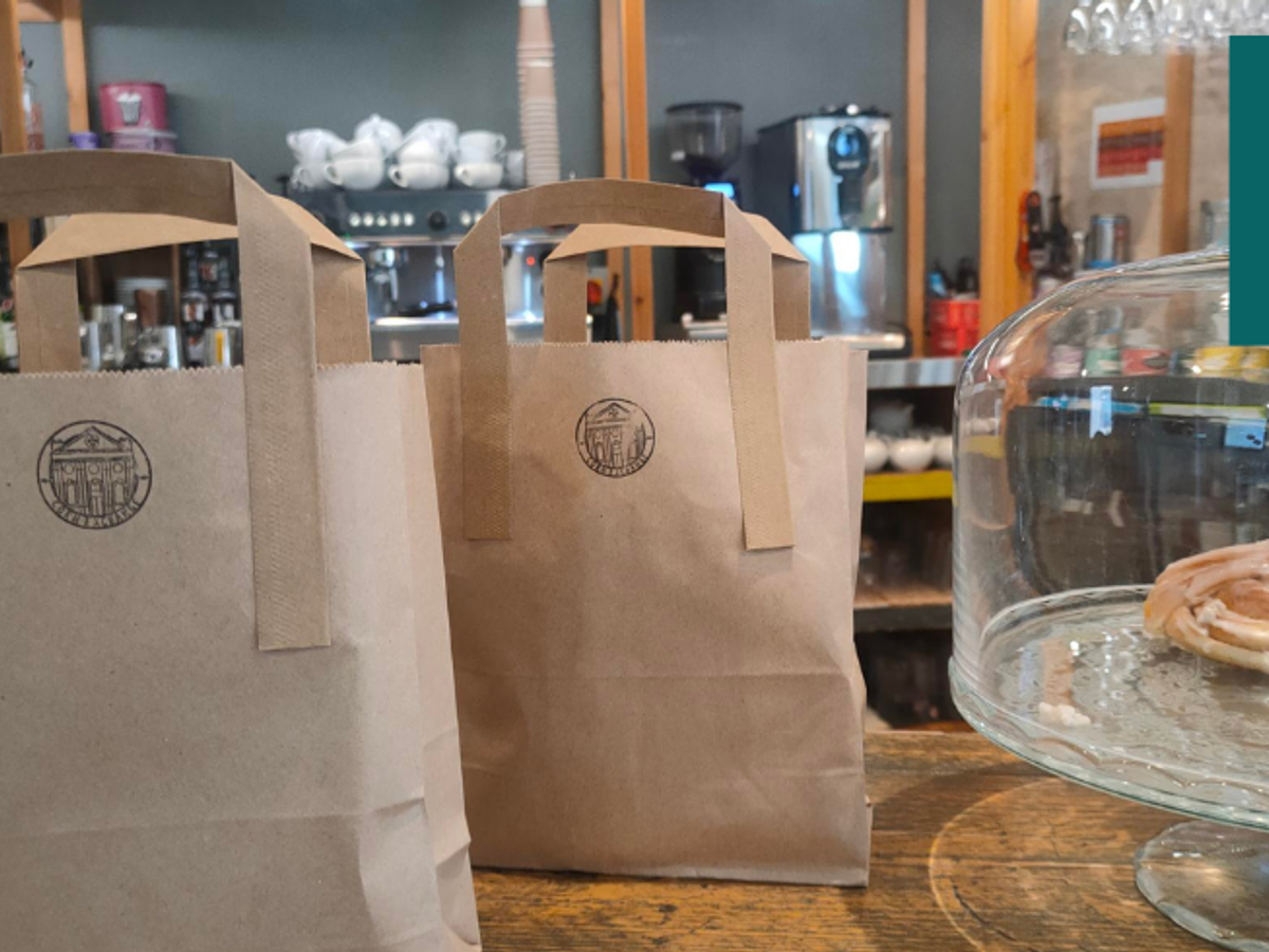 Two brown bags with a stamp of the Corn Exchange on them sit on a counter next to some baked goods