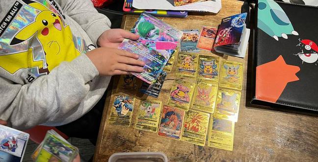 A person wearing a Pikachu jumper sorts through their Pokémon cards on a wooden table