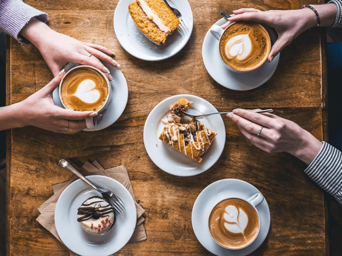 An areal view shot of two people with three coffees with latte art and three cakes on a wooden table