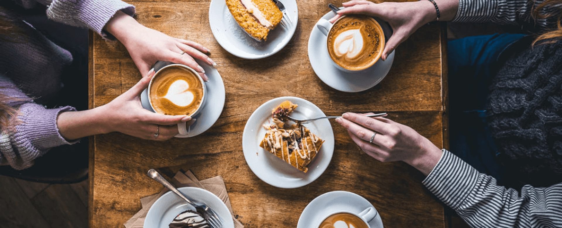An areal view shot of two people with three coffees with latte art and three cakes on a wooden table