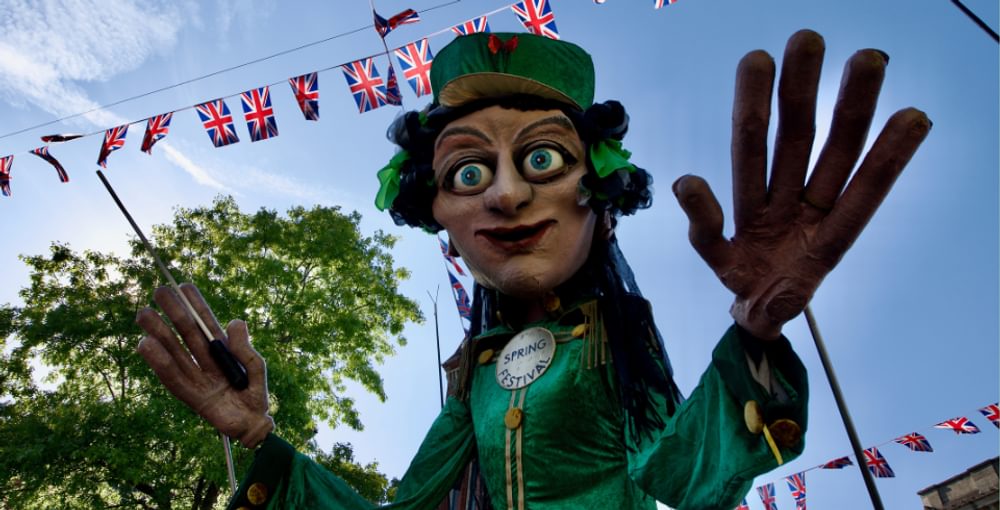 A giant puppet, wearing green and holding a conductor's baton.