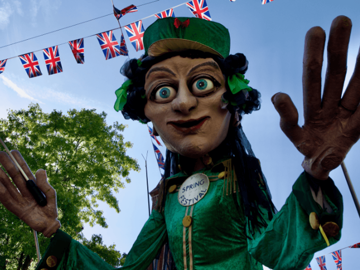 A giant puppet, wearing green and holding a conductor's baton.