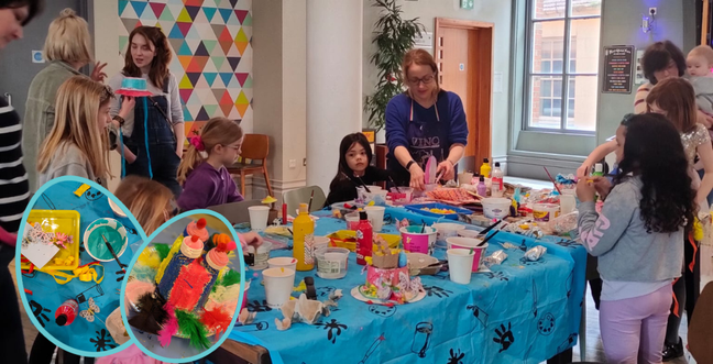 A lively Easter craft workshop with children and adults decorating bonnets using paints, feathers, and other materials. A woman in a purple apron leads the activity, while the room buzzes with creativity and conversation.