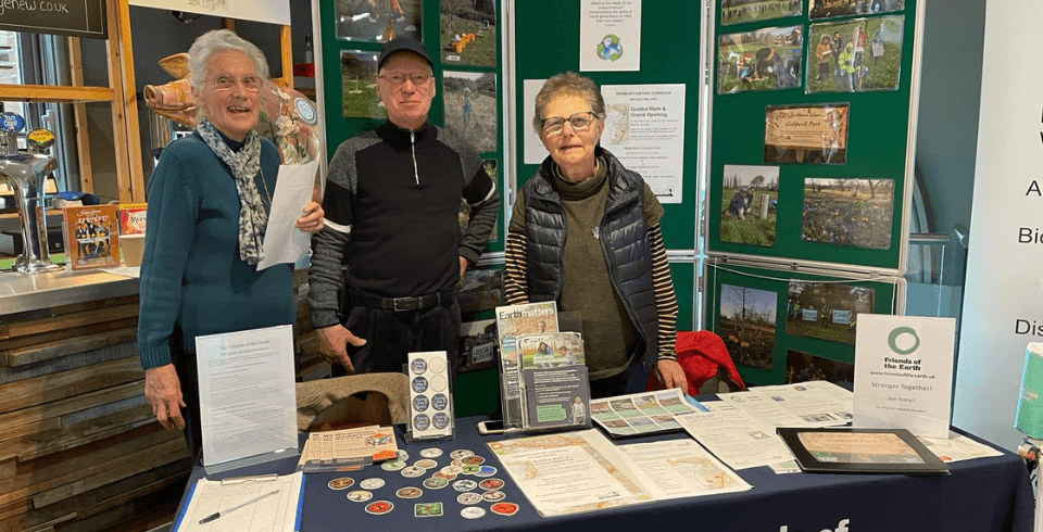 Three people stand smiling in front of a green noticeboards full of environmental facts