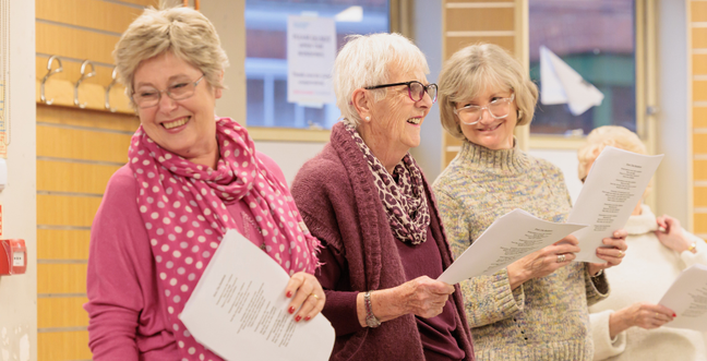 Three women stand smiling in a singing class