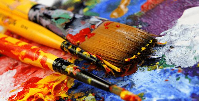 3 Paintbrushes covered in paint sit on top of a messy paint pallet