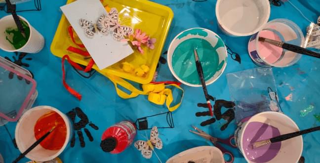A table with a blue table cloth, pots of paint and small hand prints in paint