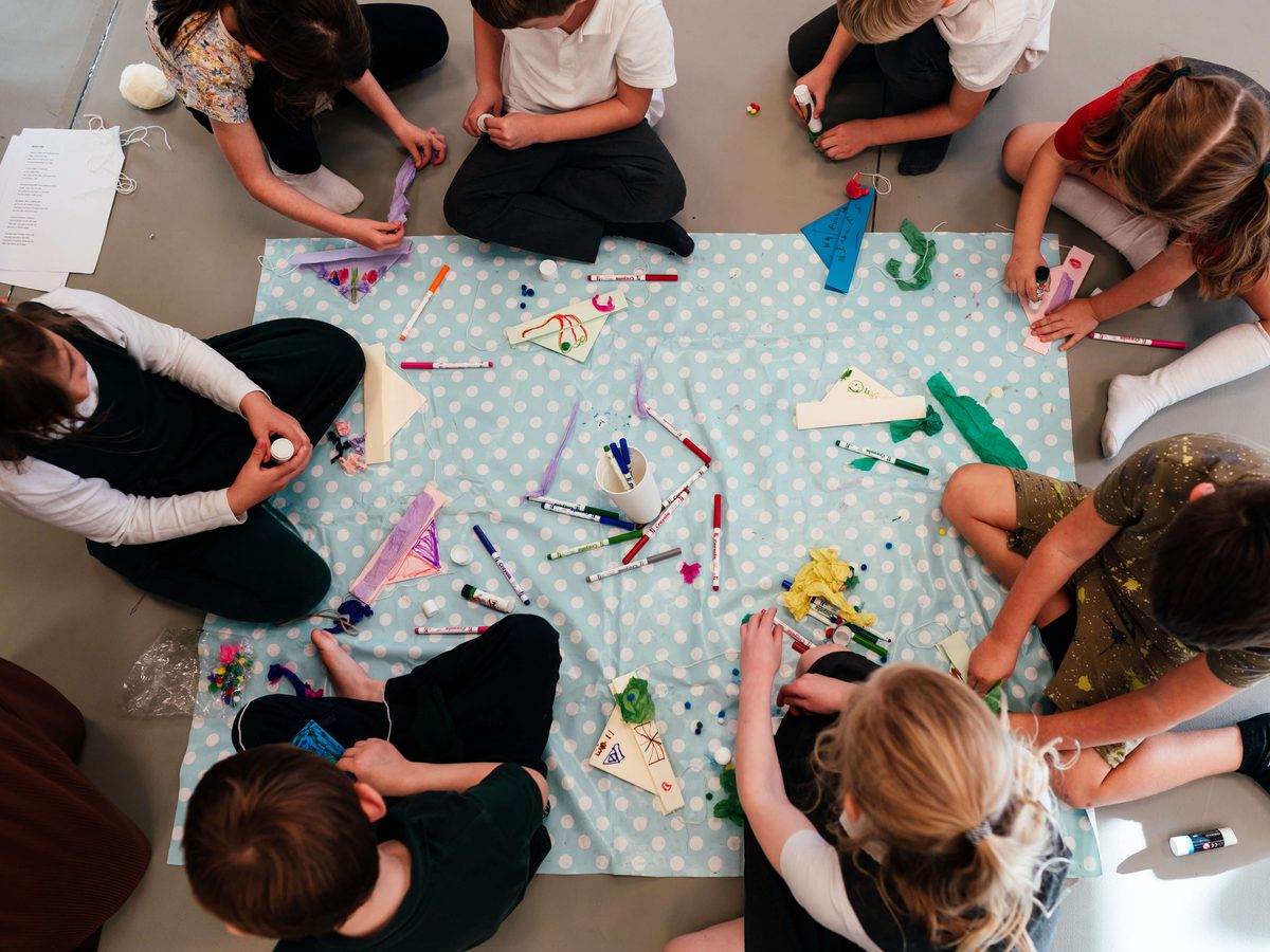 A group of children sit in a circle around a craft activity