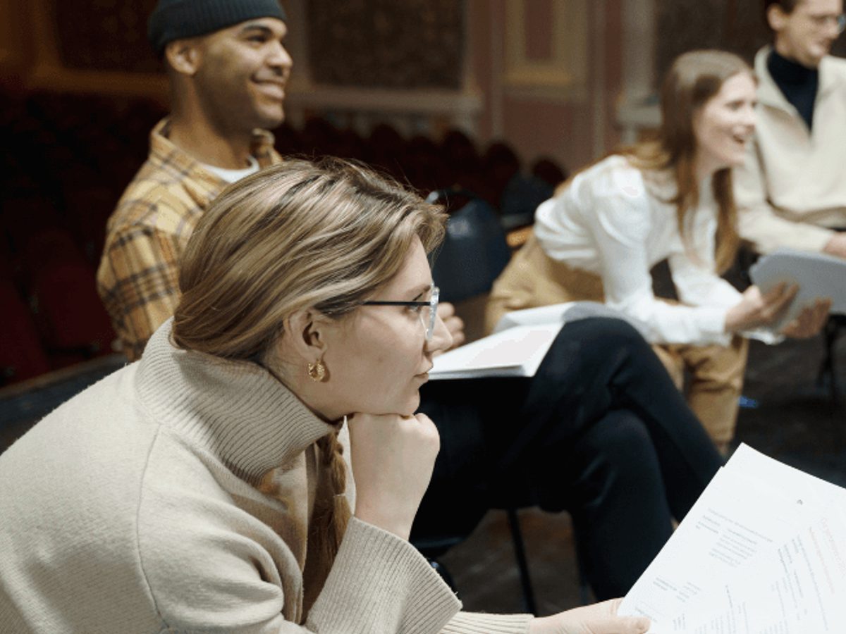 A group of adults sit listening as they read scripts as a group