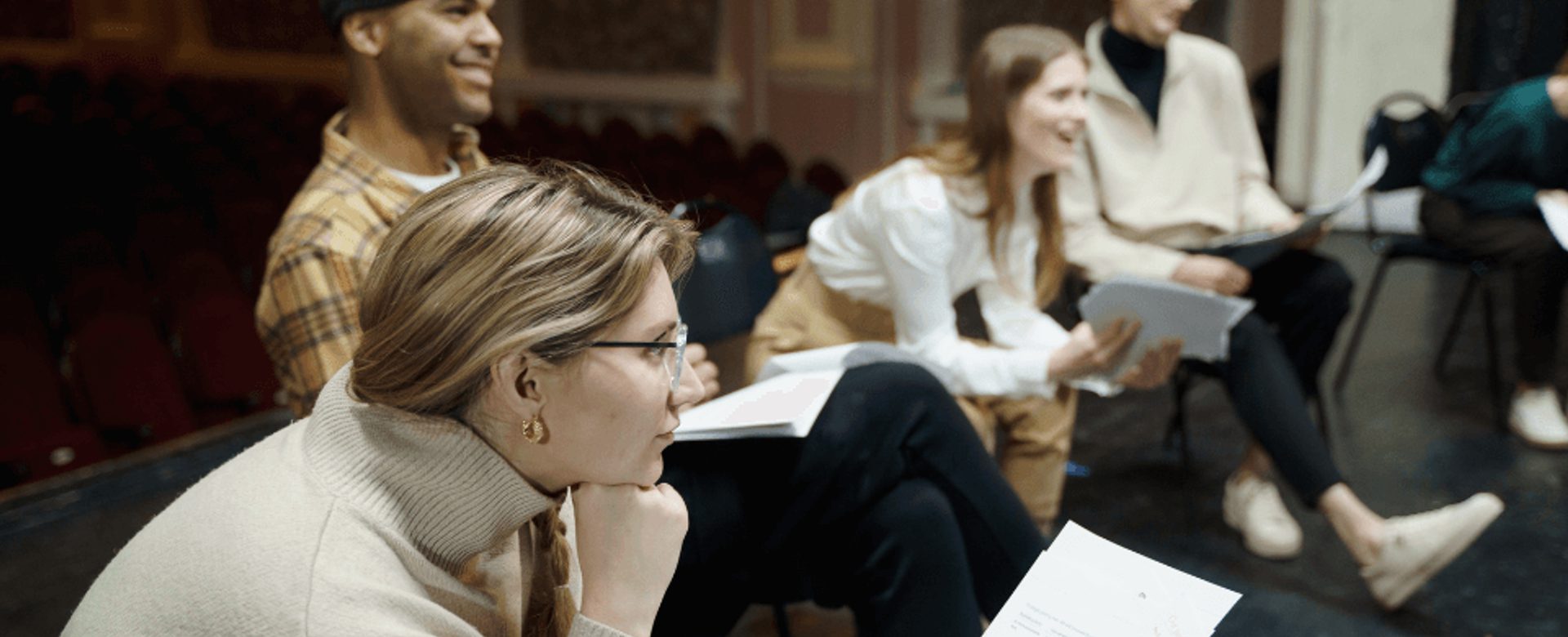A group of adults sit listening as they read scripts as a group