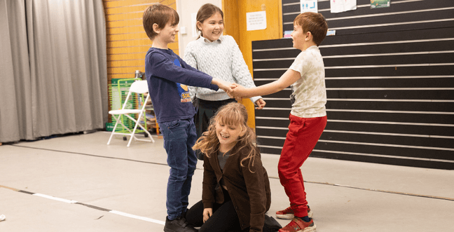 A group of kids in a room huddling around a girl sat on the floor