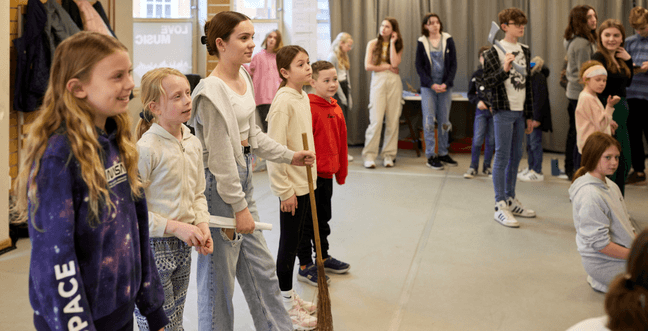 A group of children in a large room with grey flooring.