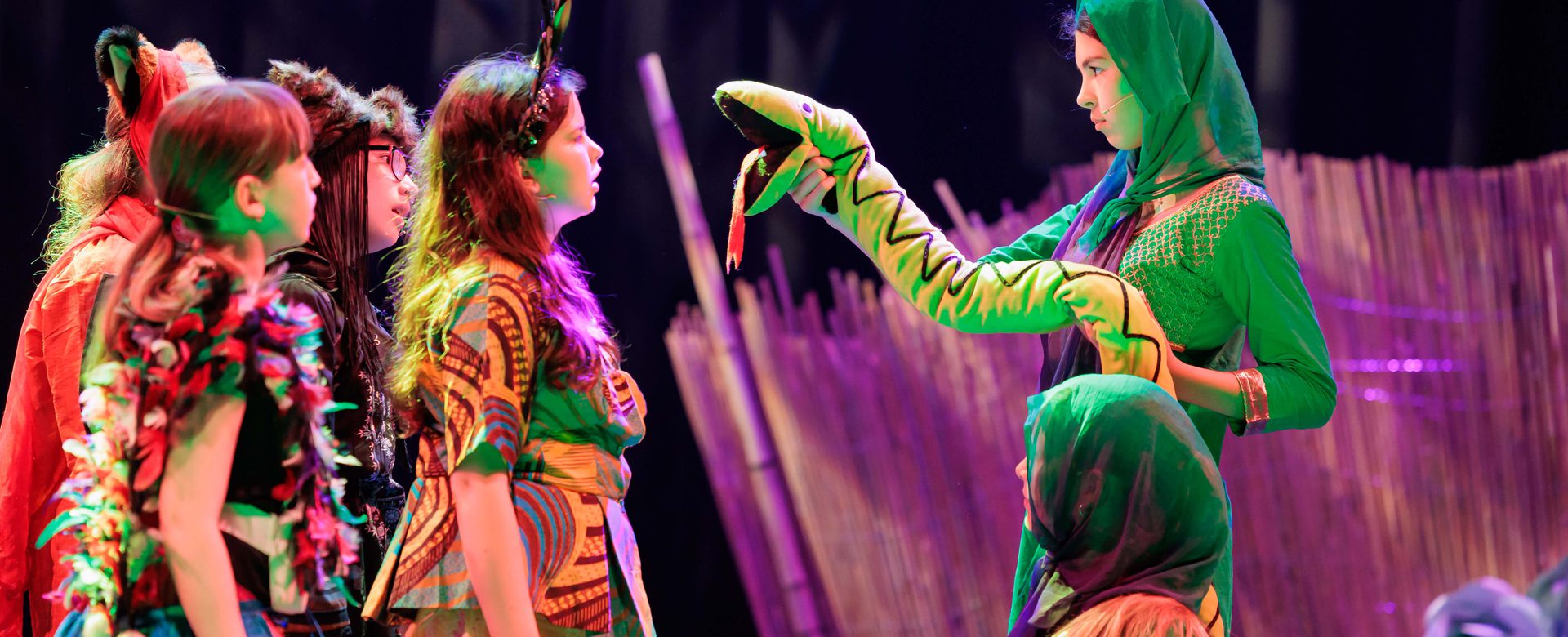 Two girls dressed in green holding a toy snake stand in front of a group of girls all dressed as various jungle animals