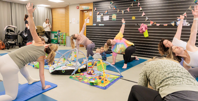 mums and their babies on yoga mats in a circle. The mums doing pilates poses while the babies play around them