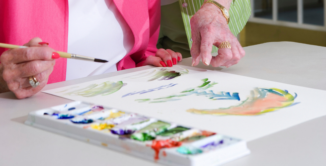 A lady paints on a large piece of paper using watercolour paint