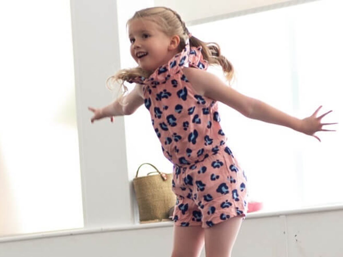 A young girl with blonde hair jumps in the air enthusiastically