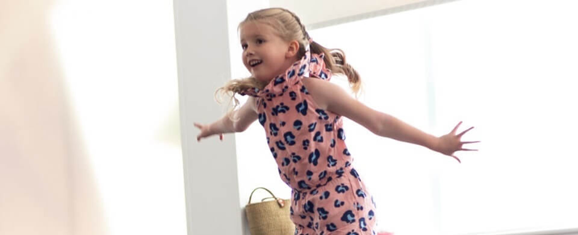 A young girl with blonde hair jumps in the air enthusiastically