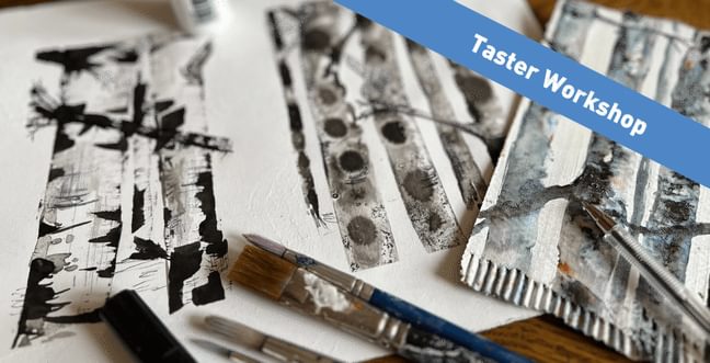 Two pieces of paper with black and white tree drawings next to a paint brushes