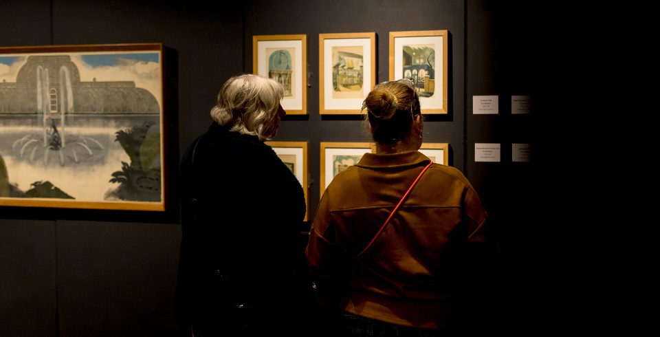 Two people looking at prints on a dark wall in a gallery