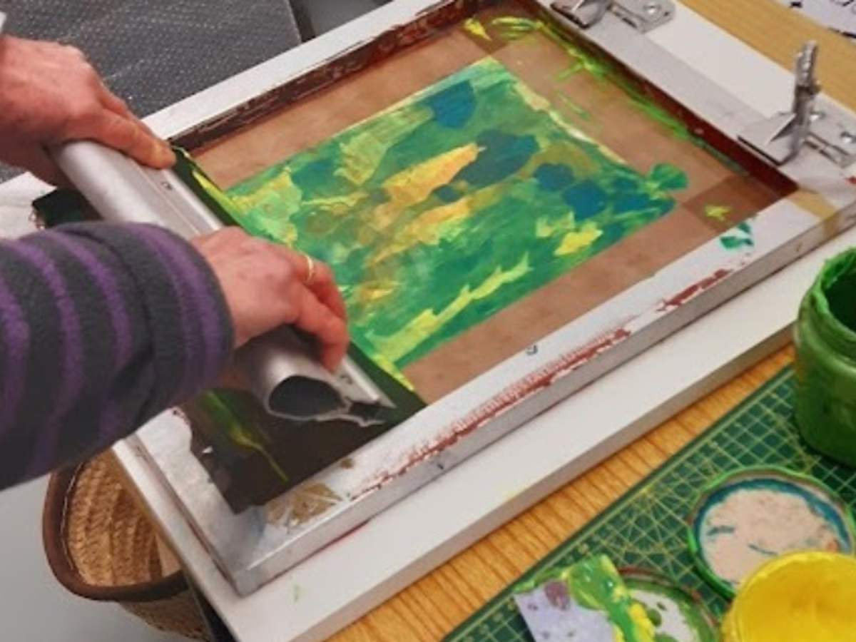 Two hand with a silk screen, printing in green and yellow ink