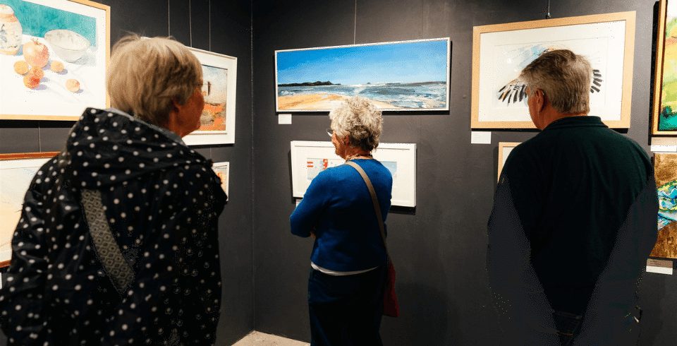 Three people looking at artwork in a gallery against a black wall