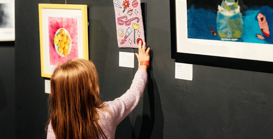 A little girl puts her hand on a painting in a gallery