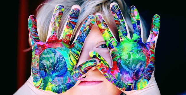 A child holds their multi-coloured paint hands over their face