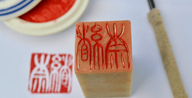 A wood tenkoku block with red ink next to a print of the design, an ink pad and pen