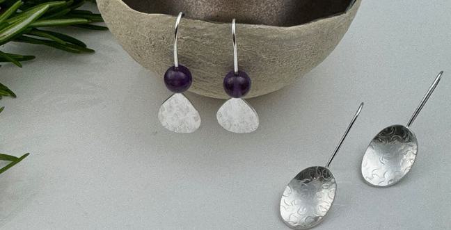 A pair of silver earrings hangs off a small bowl and another pair lie on the table top