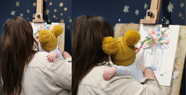 Mother holds her baby as she paints on a canvas