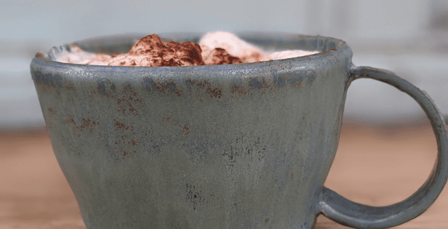 A grey handmade mug with cream and marshmallows in it.