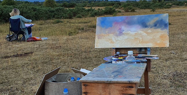 A painting with a blue and orange clouded sky on an easel in a field