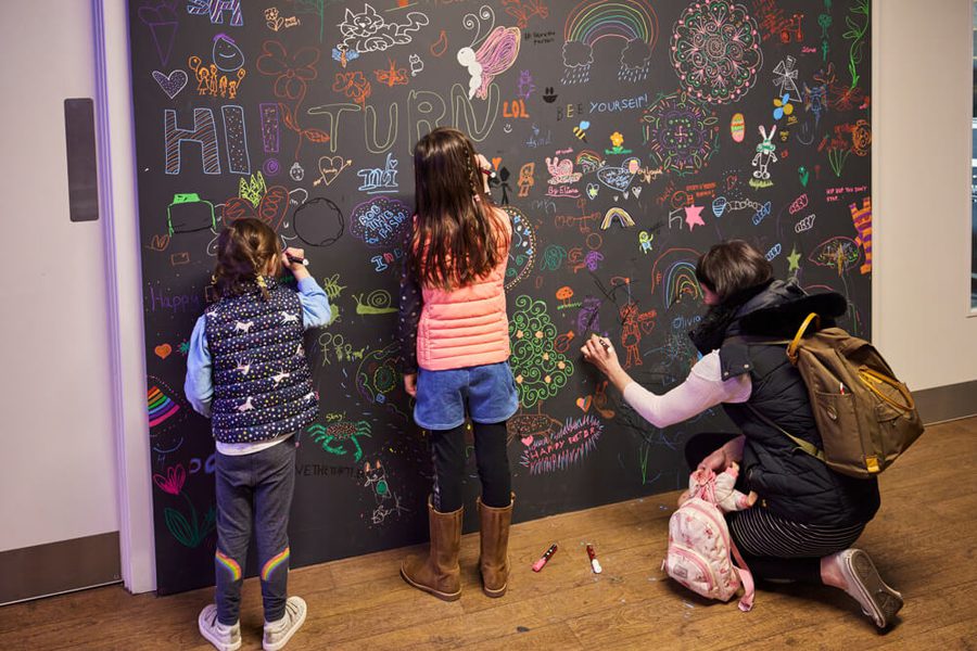 Children stand drawing on a chalkboard wall