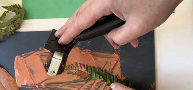 Hands with paint roller and fern leaf.