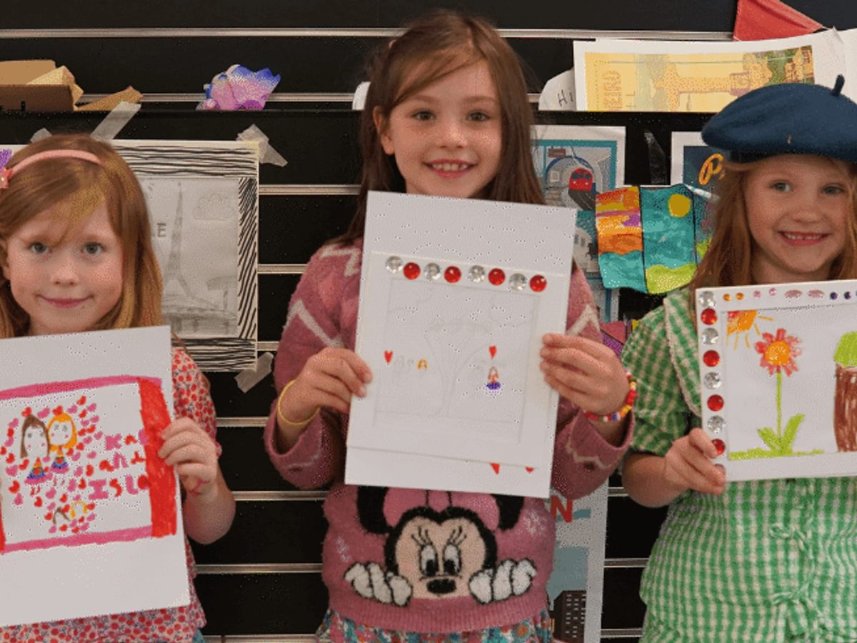 Three little girls proudly holding up their drawings.