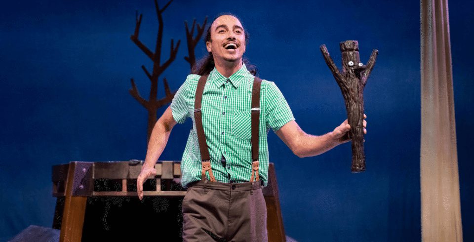 A man holding a wooden Stick Man, smiling.