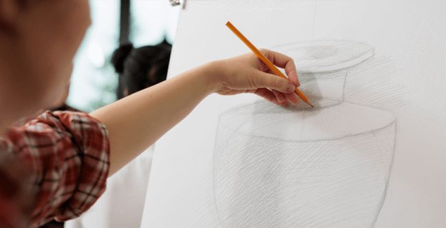 A hand holding a pencil, using it to sketch a picture of a clay pot.