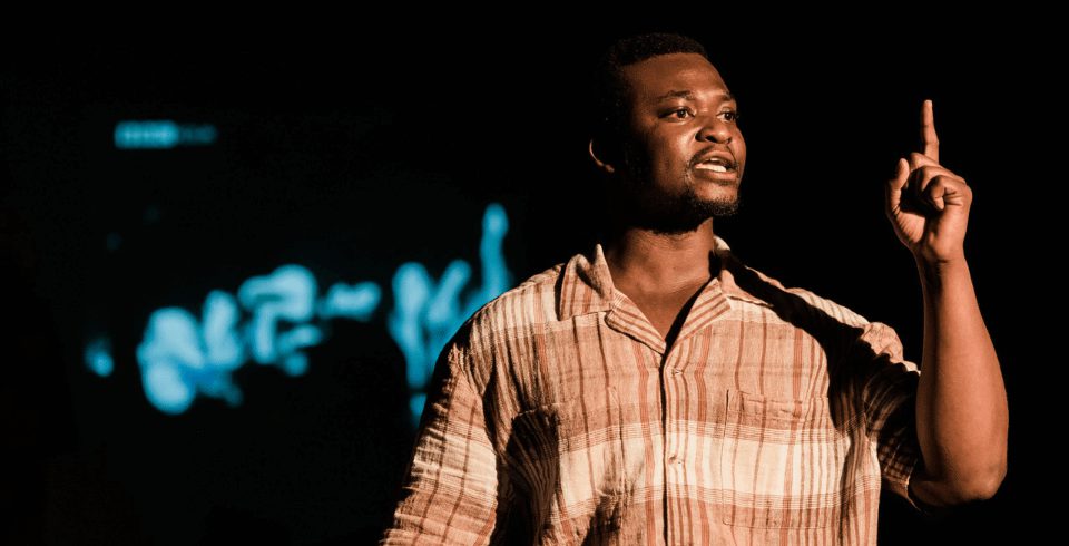 A man in a brown shirt pointing upwards.