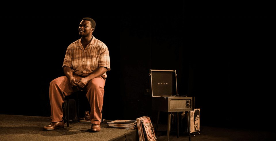 A man in a beige shirt sat on a chair next to an open case.